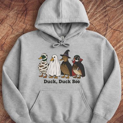 A light gray pullover hoodie laid flat on a textured brown wood background, featuring a graphic of four cartoon ducks dressed in Halloween costumes with the text 'Duck, Duck Boo' underneath.