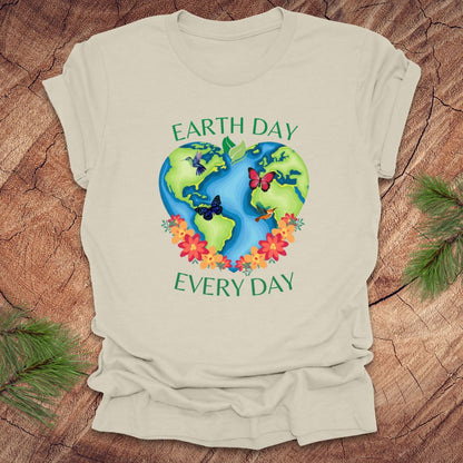 Beige t-shirt with Earth Day design featuring the Earth, flowers, and butterflies on a wooden surface.