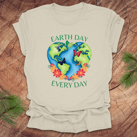 Beige t-shirt with Earth Day design featuring the Earth, flowers, and butterflies on a wooden surface.