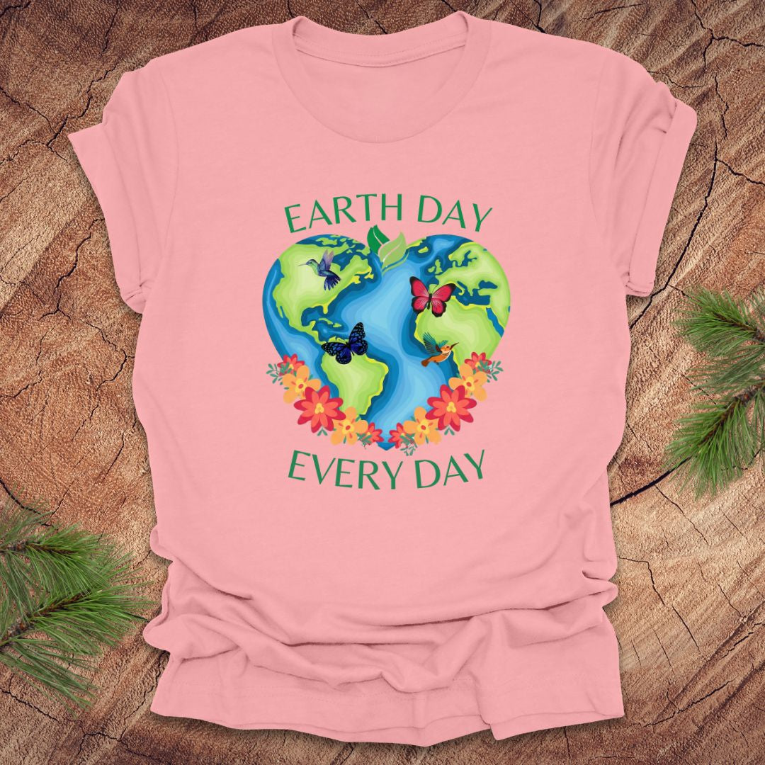 Pink t-shirt with Earth Day design featuring the Earth, flowers, and butterflies on a wooden surface.