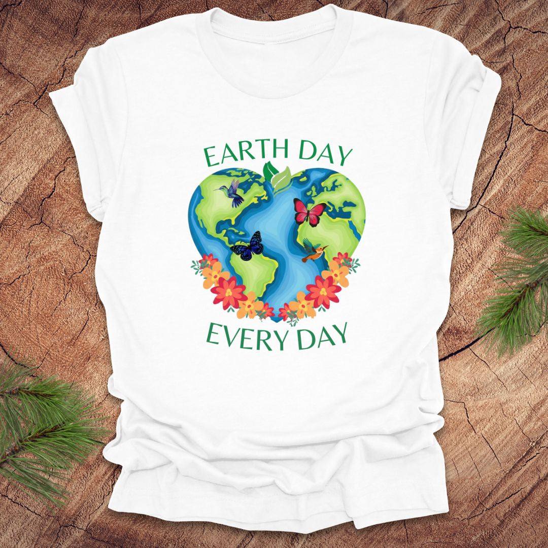 White t-shirt with Earth Day design featuring the Earth, flowers, and butterflies on a wooden surface.