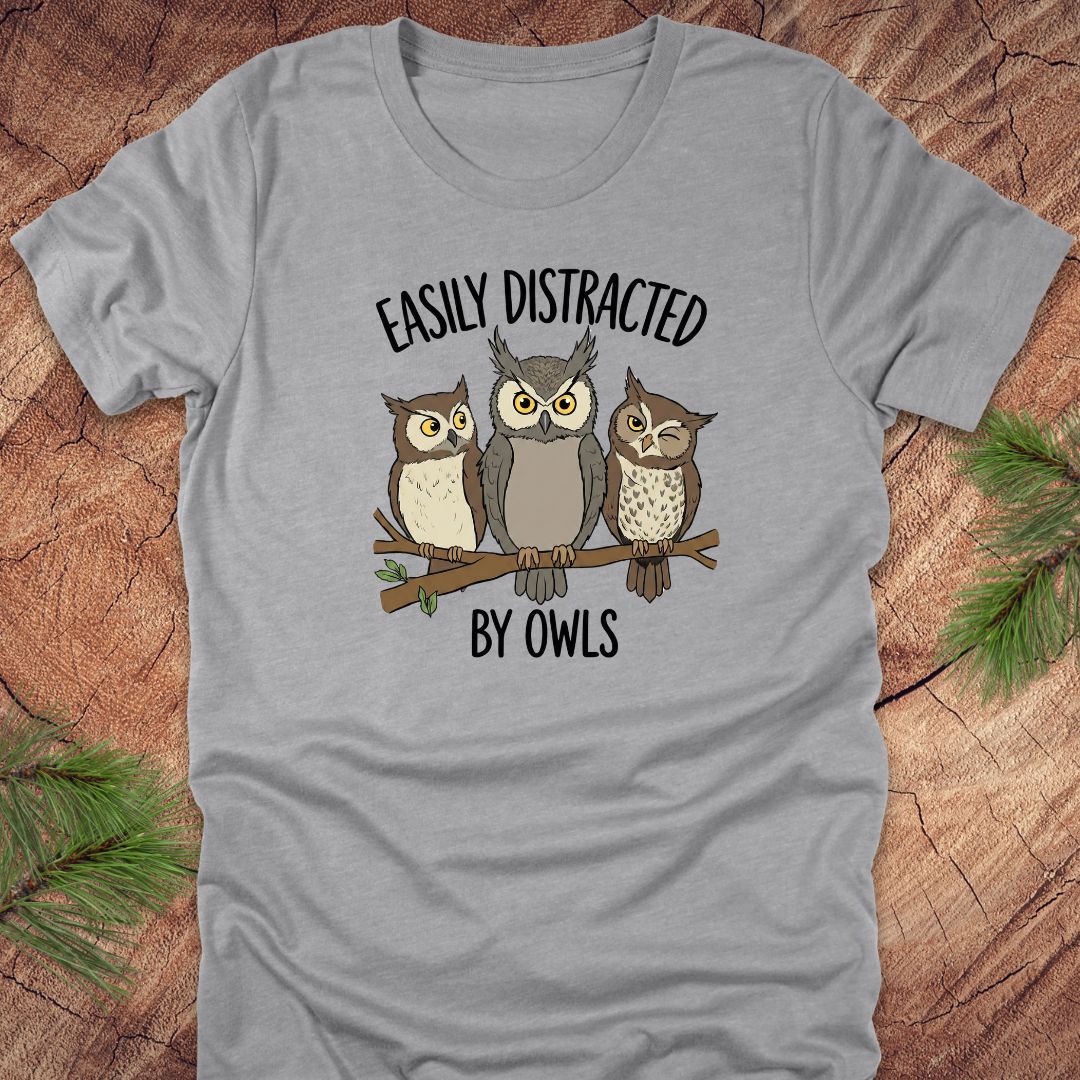 Gray t-shirt with owl design and text 'Easily Distracted by Owls' on a wooden surface.