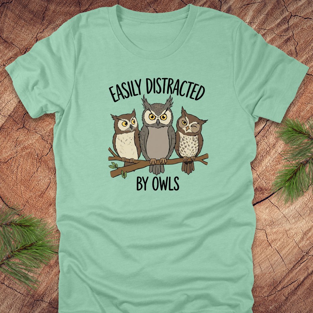Light green t-shirt with owl design and text 'Easily Distracted by Owls' on a wooden surface.