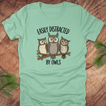 Light green t-shirt with owl design and text 'Easily Distracted by Owls' on a wooden surface.