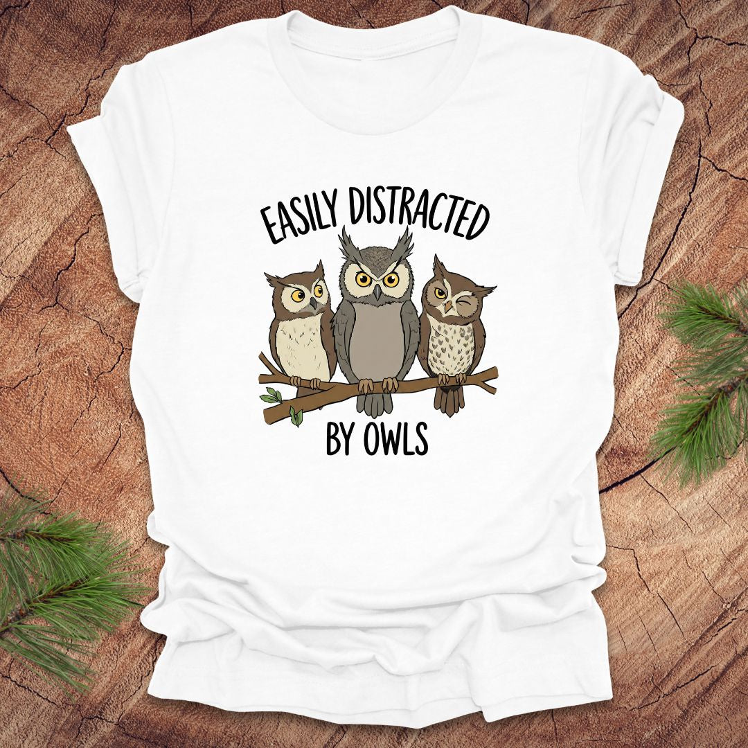 White t-shirt with owl design and text 'Easily Distracted by Owls' on a wooden surface.