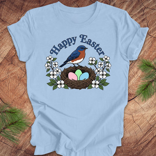 Light blue t-shirt with 'Happy Easter' design featuring a bluebird, nest, and eggs on a wooden surface.