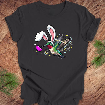 Dark gray t-shirt with a colorful design of a hummingbird with bunny ears on a wooden surface.