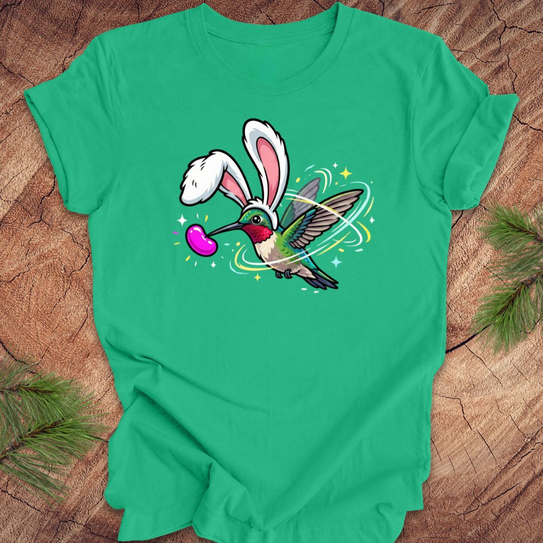 Green t-shirt with a cartoon design of a hummingbird wearing rabbit ears on a wooden surface.