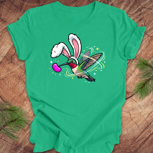 Green t-shirt with a cartoon design of a hummingbird wearing rabbit ears on a wooden surface.