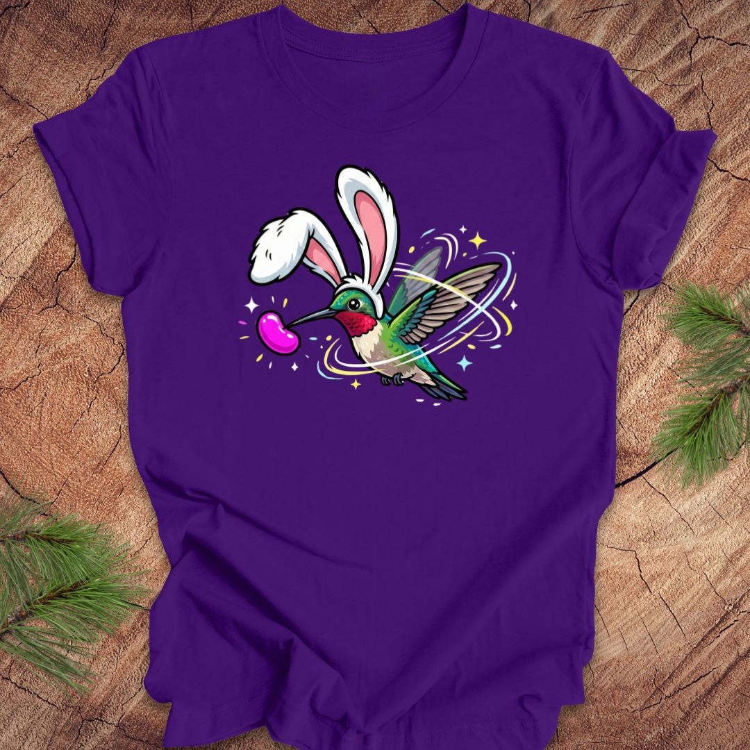 Purple t-shirt with a colorful design of a hummingbird with bunny ears on a wooden surface.