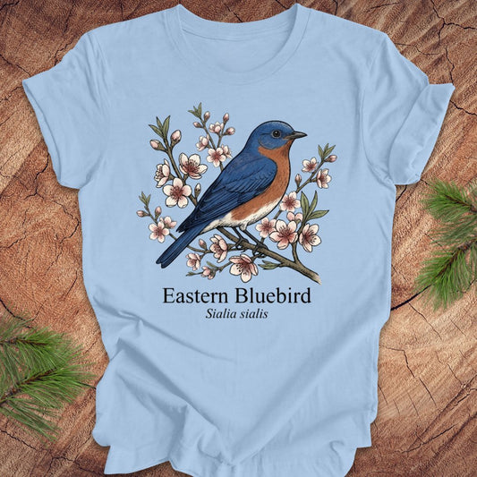 Light blue t-shirt with an illustration of an Eastern Bluebird on a wooden surface