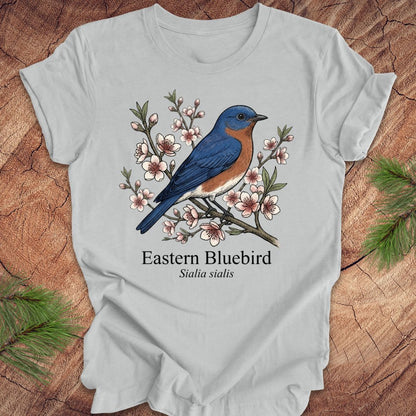 Gray t-shirt with an illustration of an Eastern Bluebird and floral design on a wooden surface.