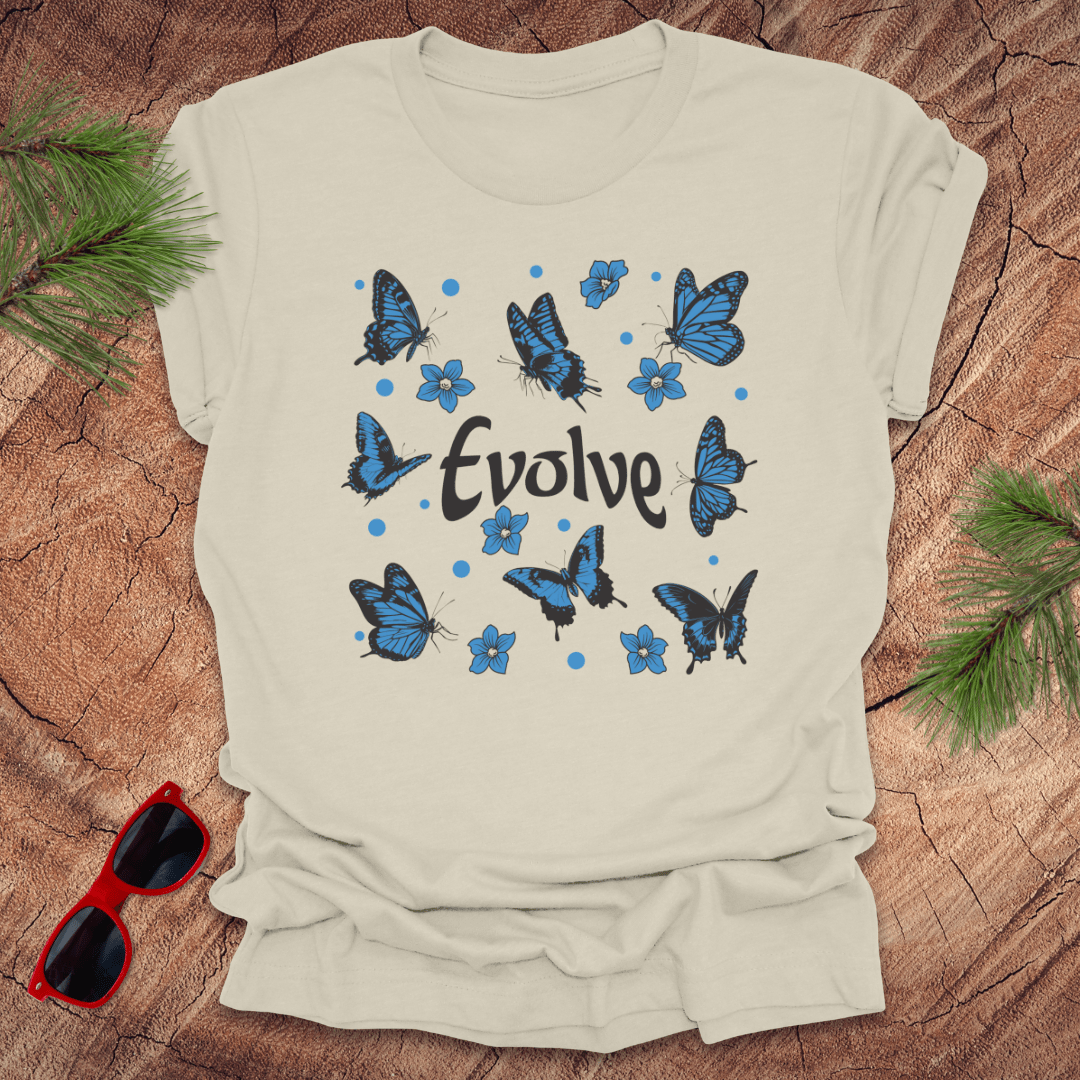 Beige t-shirt with blue butterfly design and 'Evolve' text on a wooden surface with sunglasses and greenery.