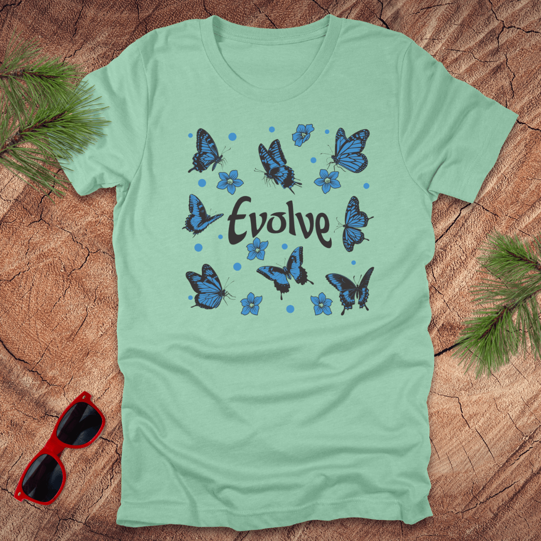 Light green t-shirt with blue butterfly design and 'Evolve' text on a wooden surface with sunglasses and leaves.