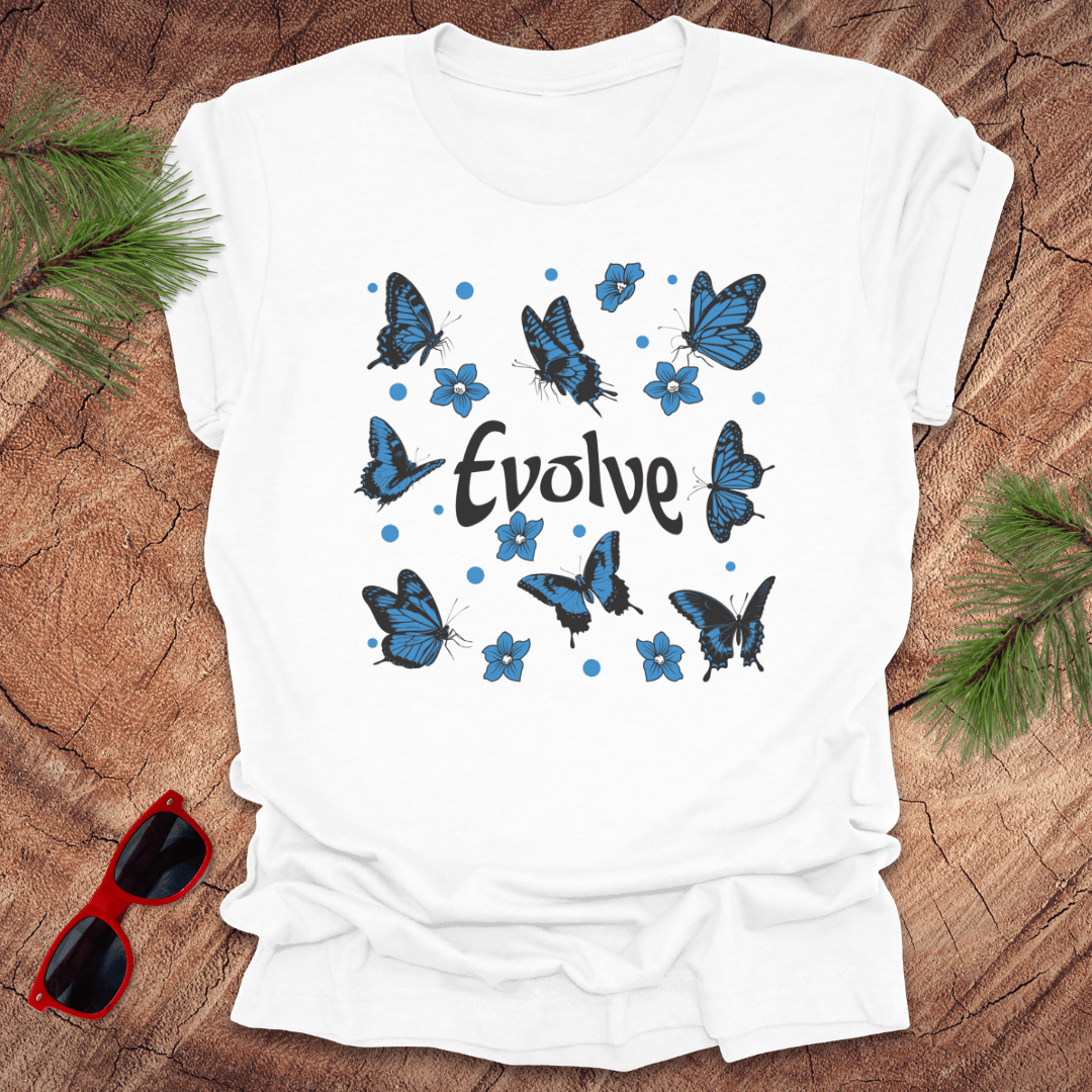 White t-shirt with blue butterfly design and 'Evolve' text on a wooden surface with sunglasses and greenery.