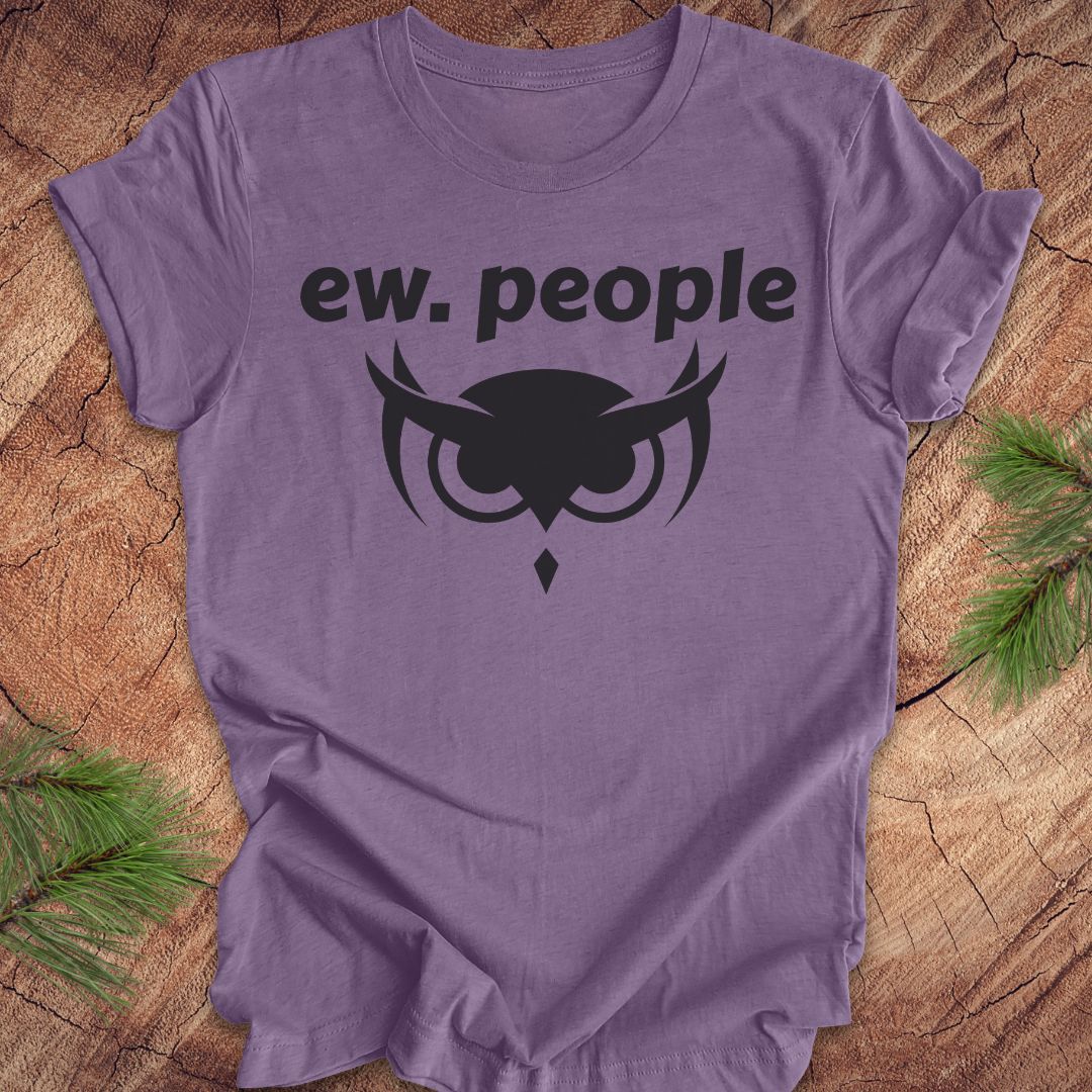 A heather purple short-sleeve t-shirt with a black graphic print reading 'ew. people' above an owl emblem, laid flat on a rustic wood background with pine branches in the corners.