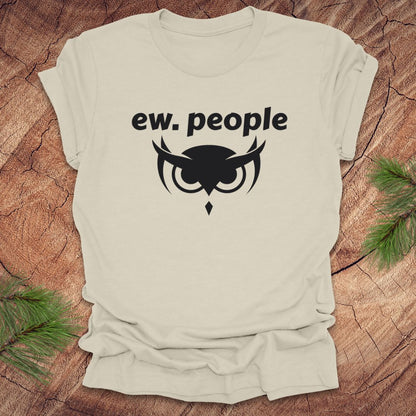 Beige t-shirt with 'ew. people' text and owl graphic on a wooden surface