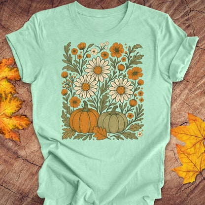 A mint green short-sleeve t-shirt with a retro autumn floral graphic, laid flat on a rustic wood background with scattered yellow and orange leaves.
