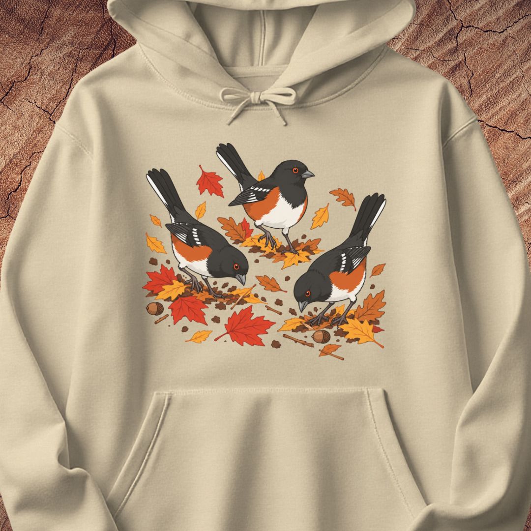 A beige hooded sweatshirt with 3 towhee birds among fall leaves, on a wood background.