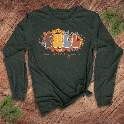 Green long-sleeve shirt with 'Fall Vibes' text on a wooden surface with pine branches.