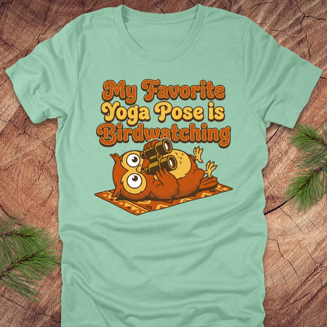 Light green t-shirt with owl design and text 'My Favorite Yoga Pose is Birdwatching' on a wooden surface.