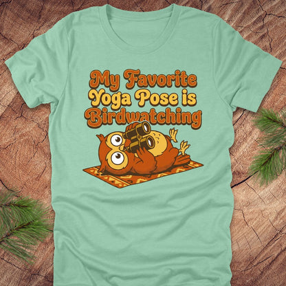 Light green t-shirt with owl design and text 'My Favorite Yoga Pose is Birdwatching' on a wooden surface.