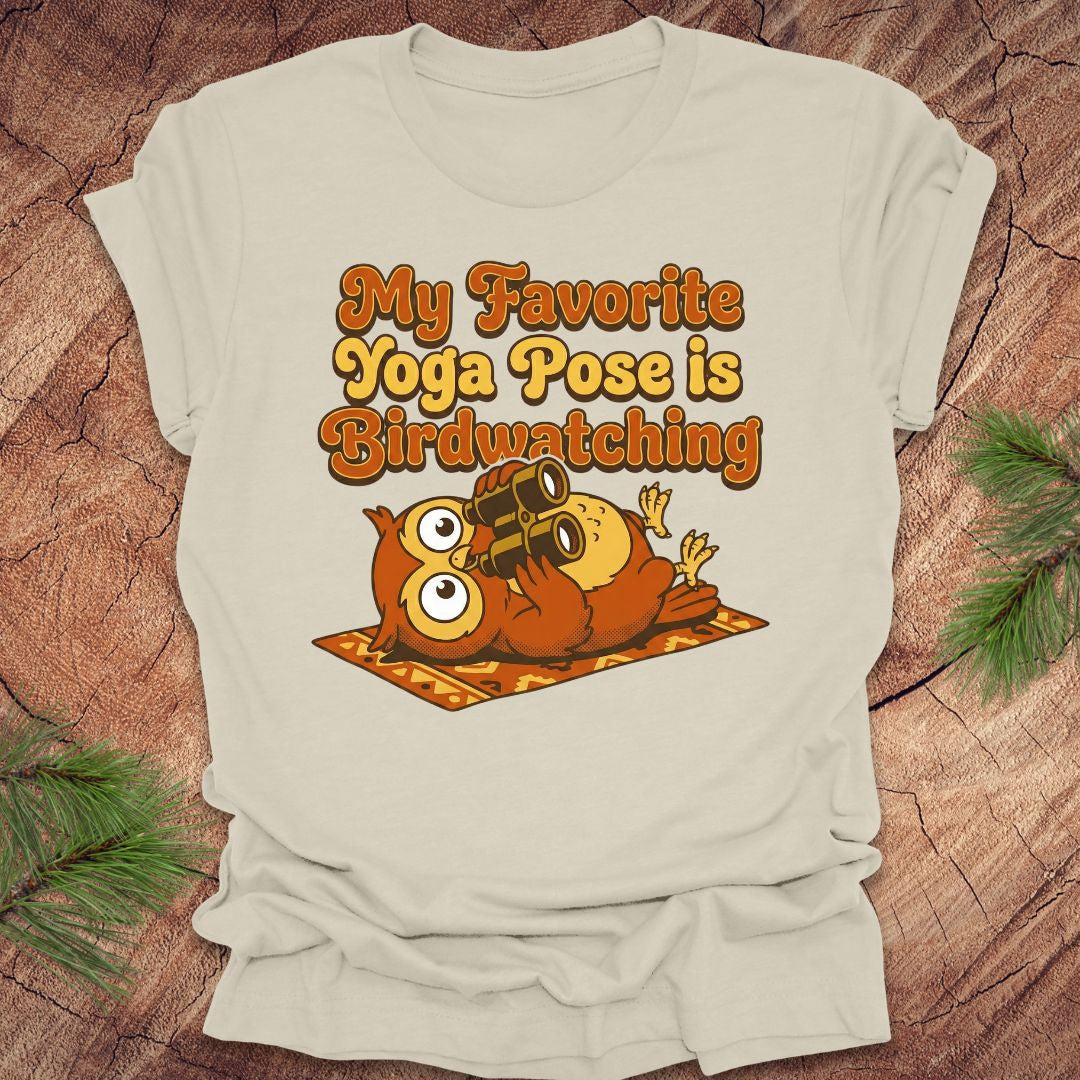Beige t-shirt with owl design and text 'My Favorite Yoga Pose is Birdwatching' on a wooden surface.