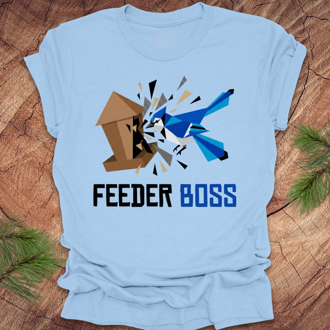 Light blue t-shirt with a graphic design of a blue bird and birdhouse with text, 'feeder boss' on a wooden surface.
