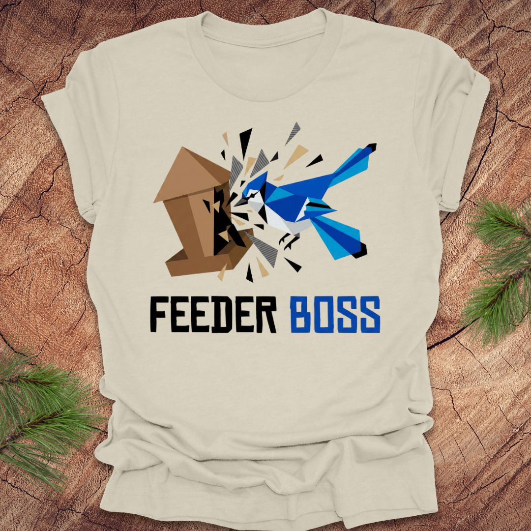 Beige t-shirt with a graphic design of a blue bird and birdhouse with text, 'feeder boss' on a wooden surface.