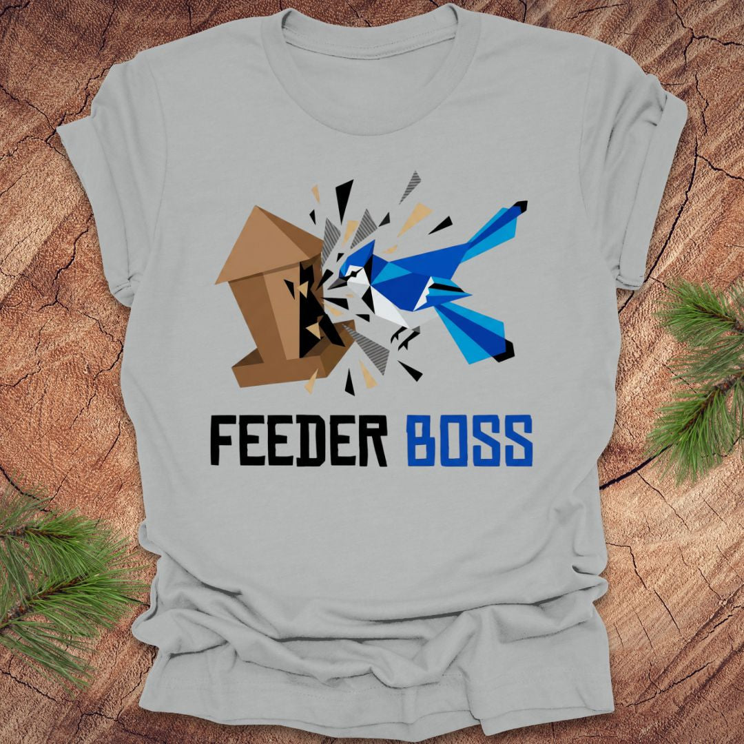 Silver t-shirt with a graphic design of a blue bird and birdhouse with text, 'feeder boss' on a wooden surface.