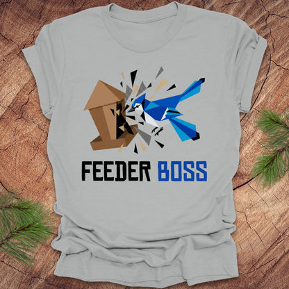 Silver t-shirt with a graphic design of a blue bird and birdhouse with text, 'feeder boss' on a wooden surface.