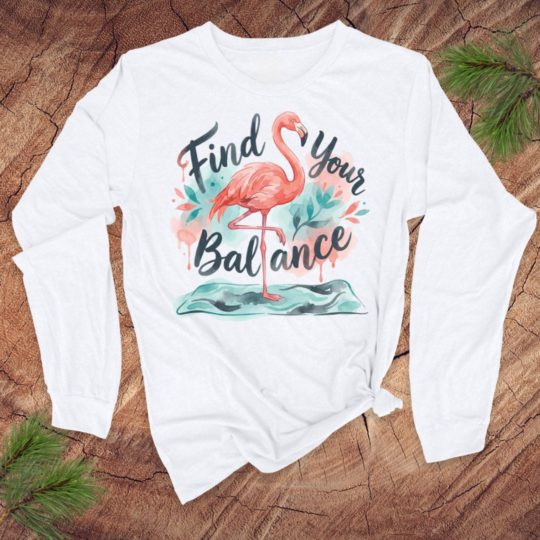 White long-sleeve shirt with flamingo graphic and text 'Find Your Balance' on a wooden surface.