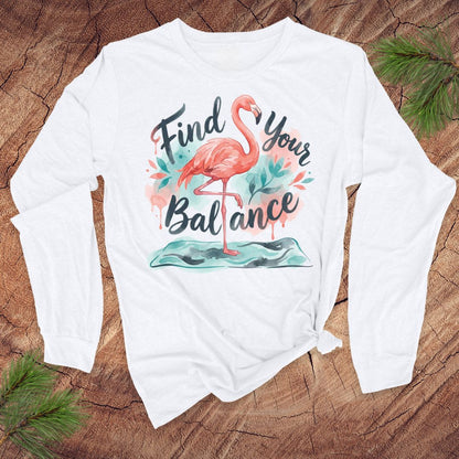 White long-sleeve shirt with flamingo graphic and text 'Find Your Balance' on a wooden surface.