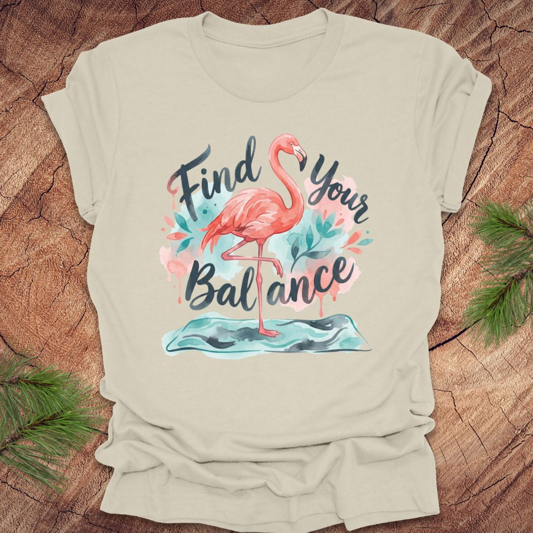 Beige t-shirt with a flamingo graphic and 'Find Your Balance' text on a wooden surface.