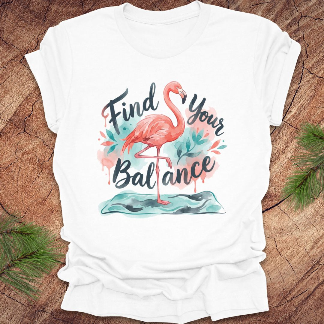 White t-shirt with a flamingo graphic and text 'Find Your Balance' on a wooden surface.