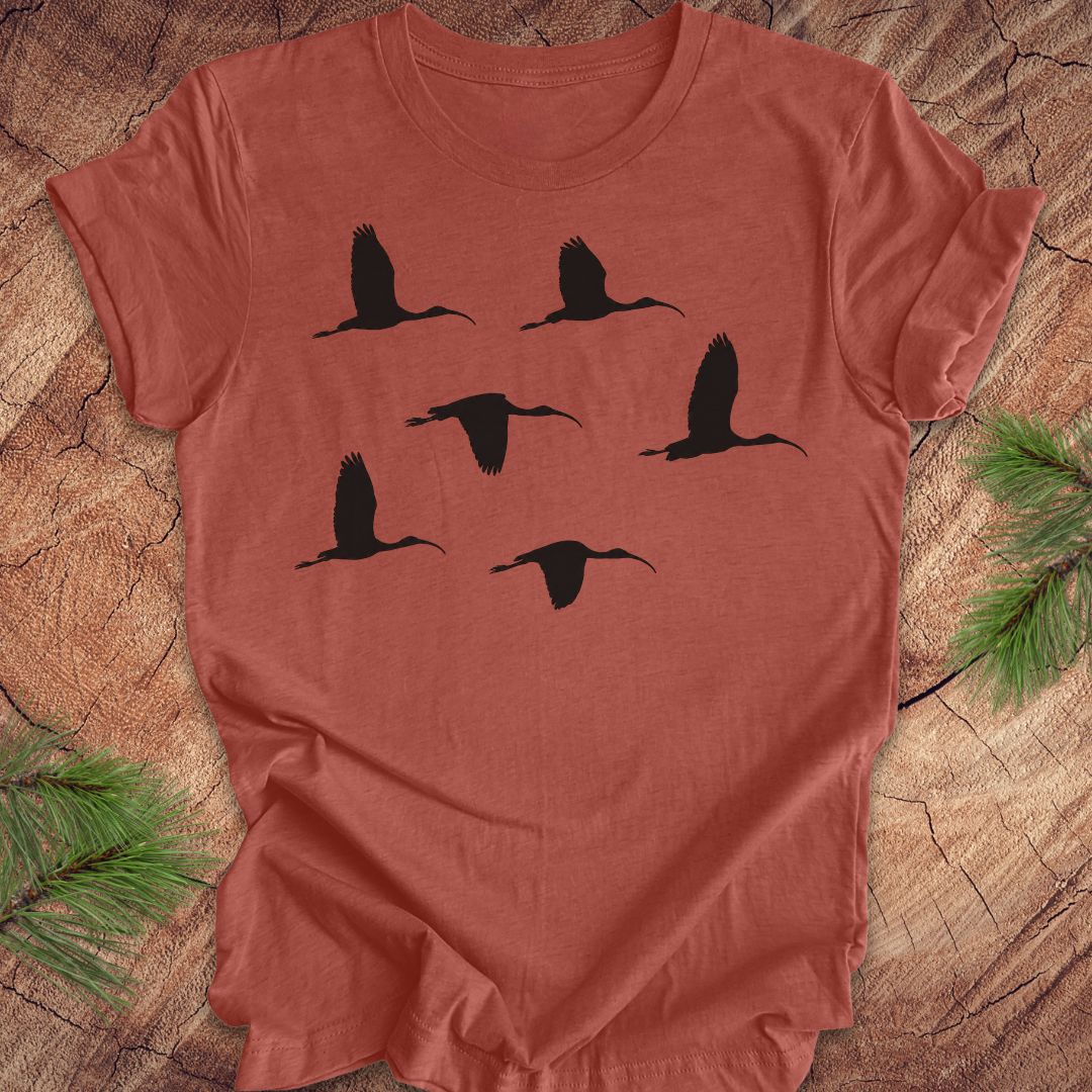 Clay colored t-shirt with black ibis bird silhouettes on a wooden surface