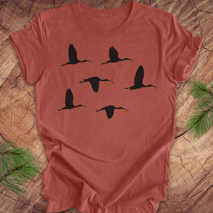 Clay colored t-shirt with black ibis bird silhouettes on a wooden surface