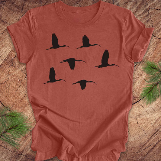 Clay colored t-shirt with black ibis bird silhouettes on a wooden surface