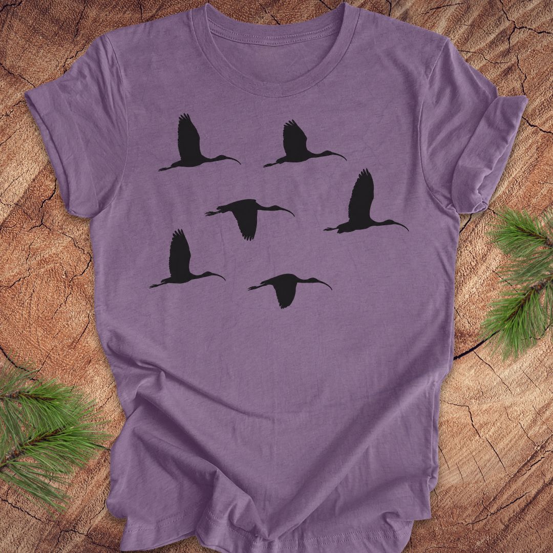Purple t-shirt with black ibis bird silhouettes on a wooden surface