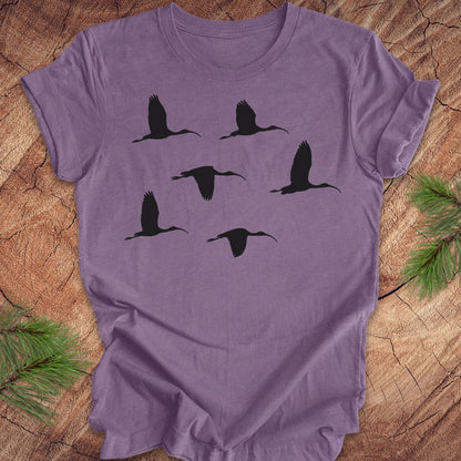 Purple t-shirt with black ibis bird silhouettes on a wooden surface