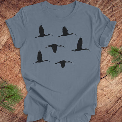 Blue t-shirt with black ibis bird silhouettes on a wooden surface