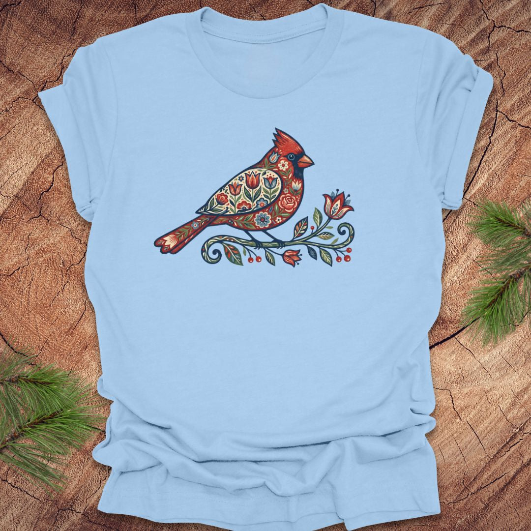 Baby blue t-shirt with a colorful cardinal and flower design on a wooden surface