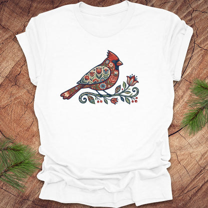 White t-shirt with a colorful cardinal and flower design on a wooden surface