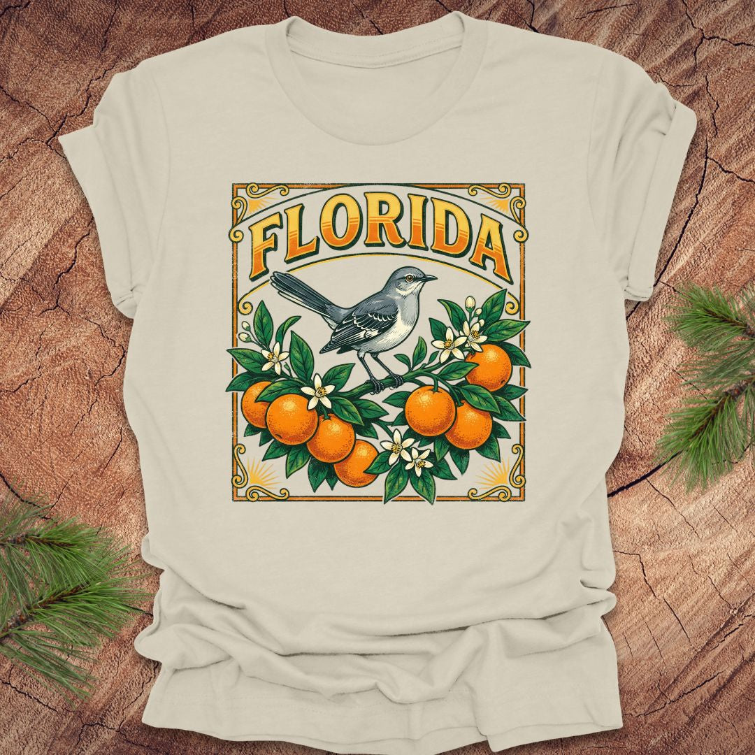 Beige t-shirt with a colorful Florida design with a mockingbird and oranges on a wood background.