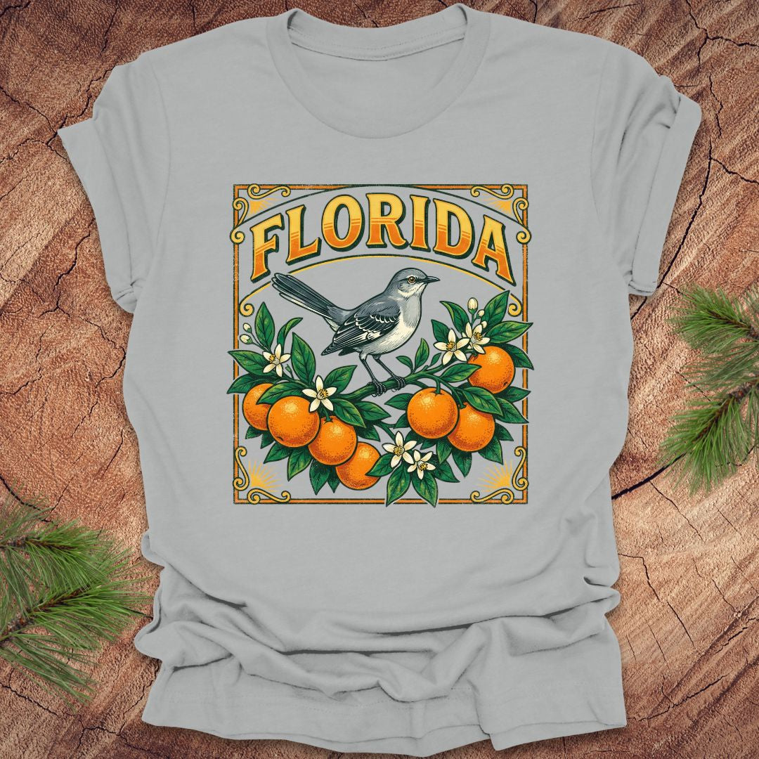 Silver t-shirt with a colorful Florida design with a mockingbird and oranges on a wood background.