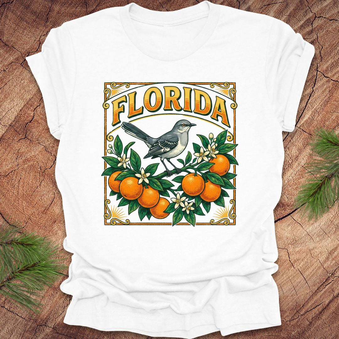 White t-shirt with a colorful Florida design with a mockingbird and oranges on a wood background.