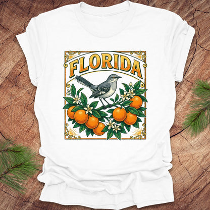 White t-shirt with a colorful Florida design with a mockingbird and oranges on a wood background.