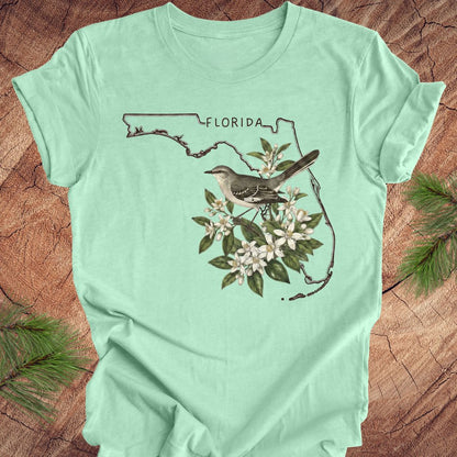 Mint green t-shirt with Florida map and bird design on a wooden surface