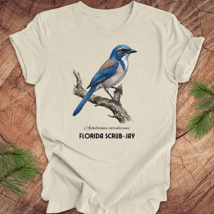 Beige t-shirt with a Florida Scrub-Jay design on a wooden surface with greenery.