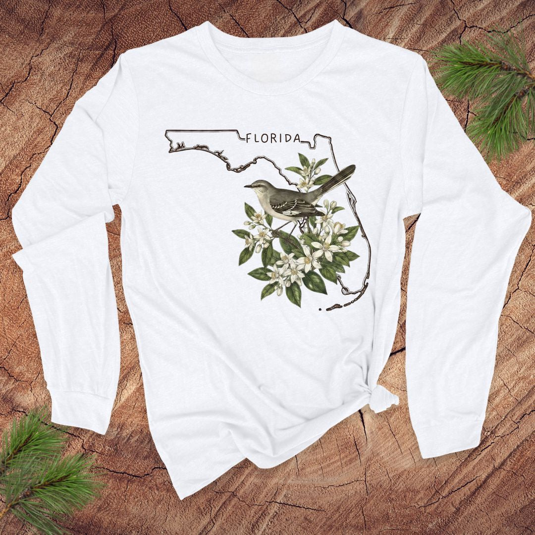 White long-sleeve shirt with Florida map and mockingbird design on a wooden surface